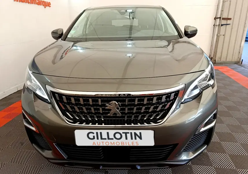 Vue de face d'un Peugeot 3008 gris foncé avec calandre chromée et phares LED allumés en intérieur showroom.