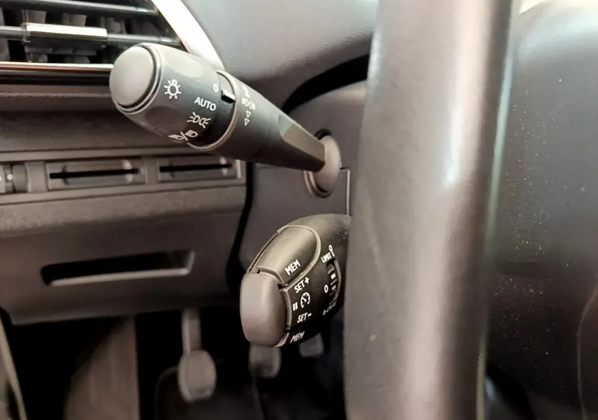Gros plan sur les commandes de régulateur de vitesse et éclairage à gauche du volant cuir du Peugeot 3008 gris foncé 2020.