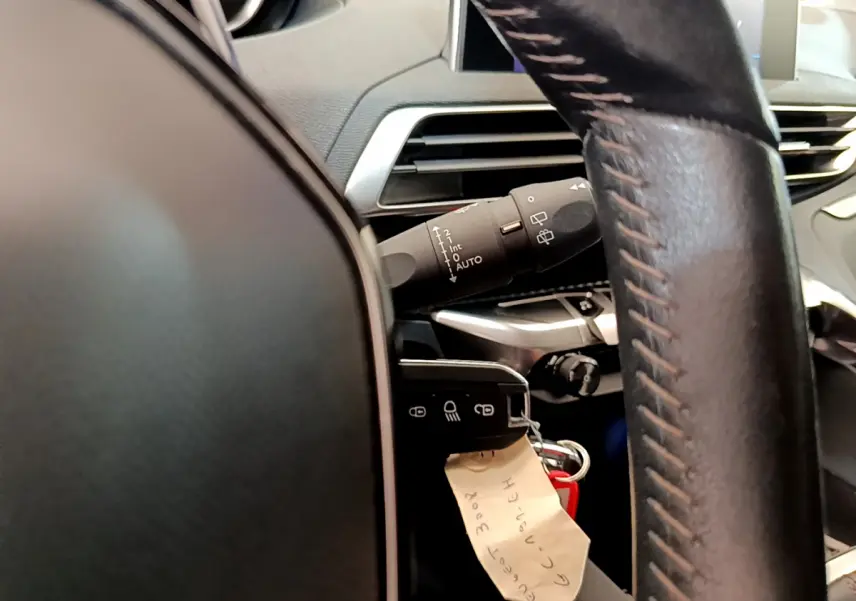 Gros plan intérieur sur le volant cuir et la commande des essuie-glaces d’un Peugeot 3008 gris foncé, version Puretech 130 S&S ACTIVE.