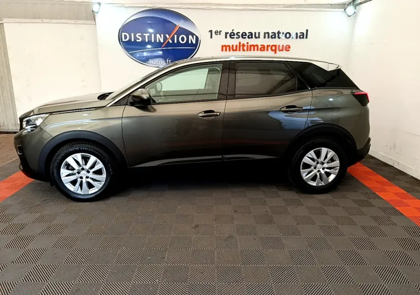 Peugeot 3008 gris foncé vue de profil côté gauche, stationnée en intérieur sur sol à damiers gris et rouge.