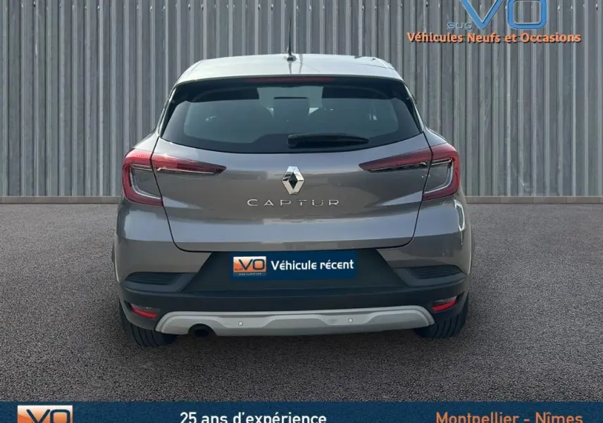 Vue arrière d'un Renault Captur gris 2020 avec feux arrière allumés sur fond urbain neutre.