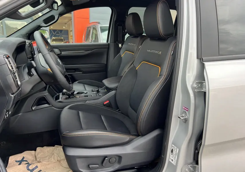 Vue intérieure côté conducteur du Ford Ranger Wildtrak X gris iconic, sièges noirs avec surpiqûres orange et logo Wildtrak X brodé.