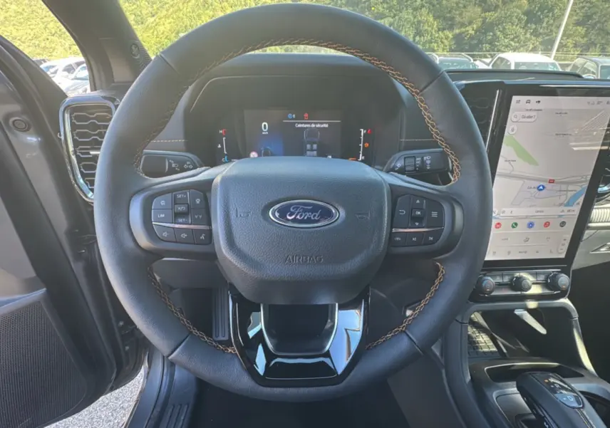 Vue intérieure centrée sur le volant cuir noir avec coutures marron du Ford Ranger 2025, écran tactile et tableau de bord numériques visibles.