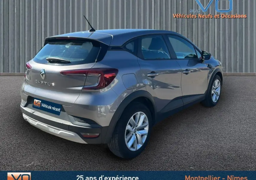 Vue 3/4 arrière droite d'un Renault Captur gris 2021 garé devant un mur métallique.