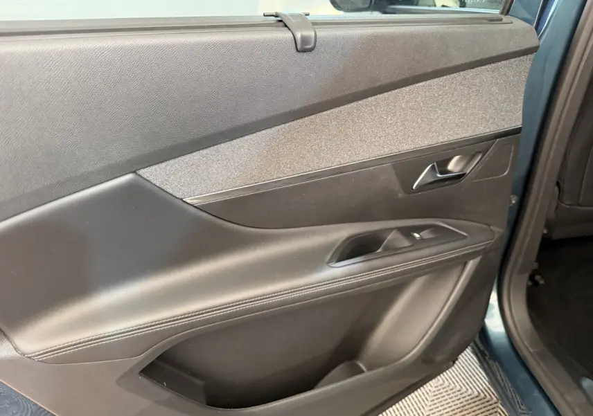 Vue intérieure du panneau de porte arrière droite du Peugeot 5008 bleu, avec poignée argentée et commandes de fenêtre.