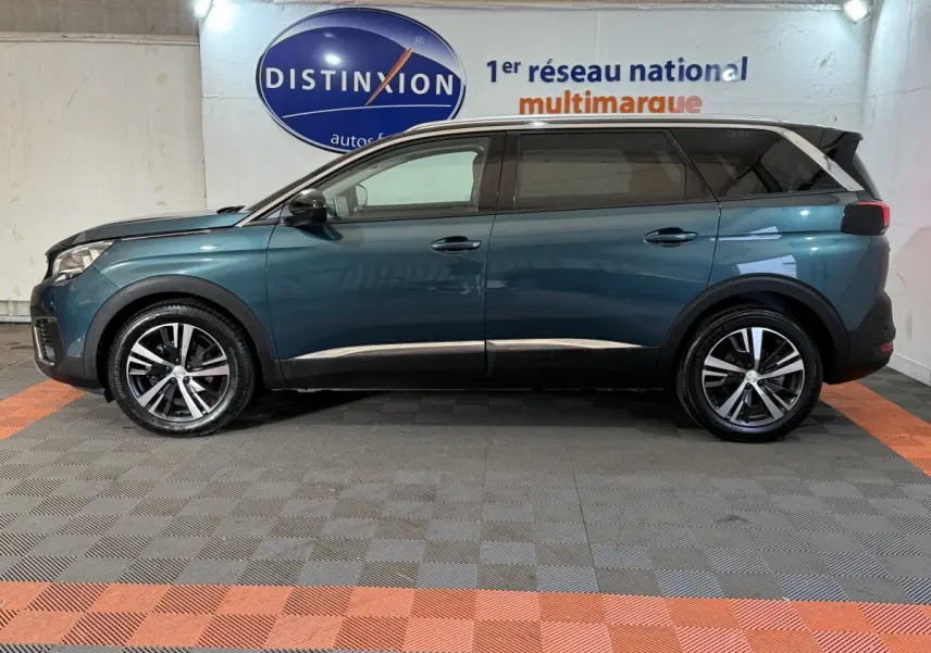 Vue de profil côté gauche d’un Peugeot 5008 bleu avec jantes alliage et vitres teintées dans un showroom intérieur.
