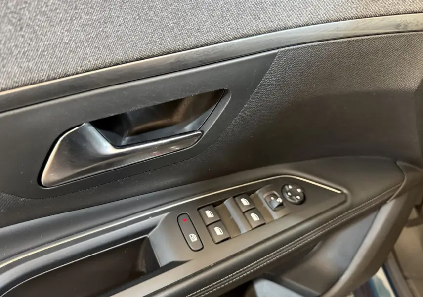 Gros plan sur la porte côté conducteur du Peugeot 5008 bleu, montrant les commandes électriques des vitres et le bouton de verrouillage.