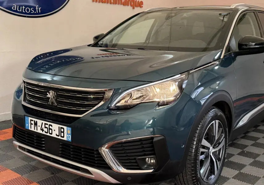Vue 3/4 avant d’un Peugeot 5008 bleu métallisé avec phares allumés et jantes alliage distinctives.