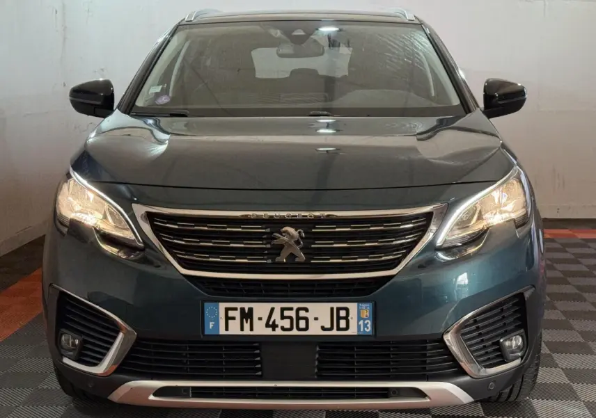 Vue avant d’un Peugeot 5008 bleu 2019 avec calandre chromée et phares allumés dans un garage.