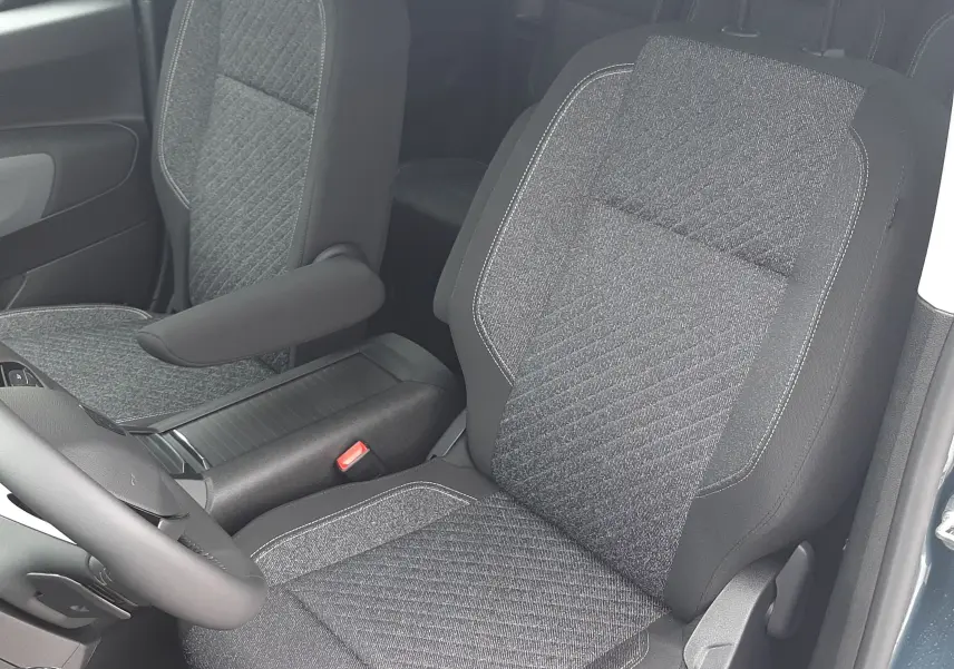 Vue intérieure du Peugeot Rifter 2026 montrant les sièges avant en tissu gris avec accoudoir côté droit, porte ouverte côté conducteur.