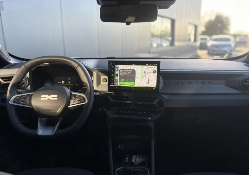 Vue frontale intérieure du tableau de bord du Dacia Duster 2026 avec écran tactile central et volant multifonction noir.