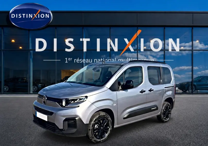 Citroën Berlingo Steel Grey vue 3/4 avant droit, avec jantes noires et barres de toit visibles devant un showroom Distinxion.