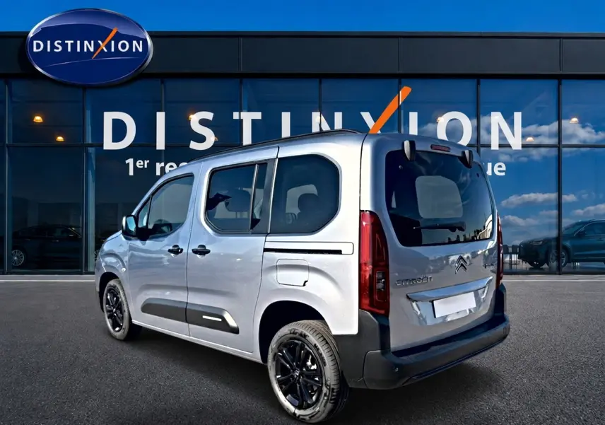 Vue 3/4 arrière droite d'un Citroën Berlingo gris acier avec jantes noires, portes latérales vitrées et logo visible.