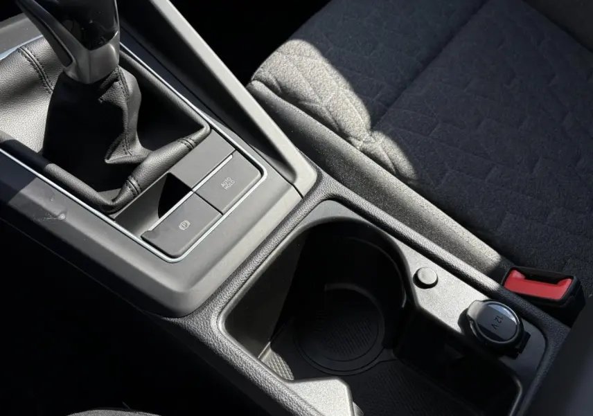 Gros plan sur la console centrale noire avec levier de vitesse manuel et porte-gobelet du Volkswagen Golf VIII Gris Lunaire.