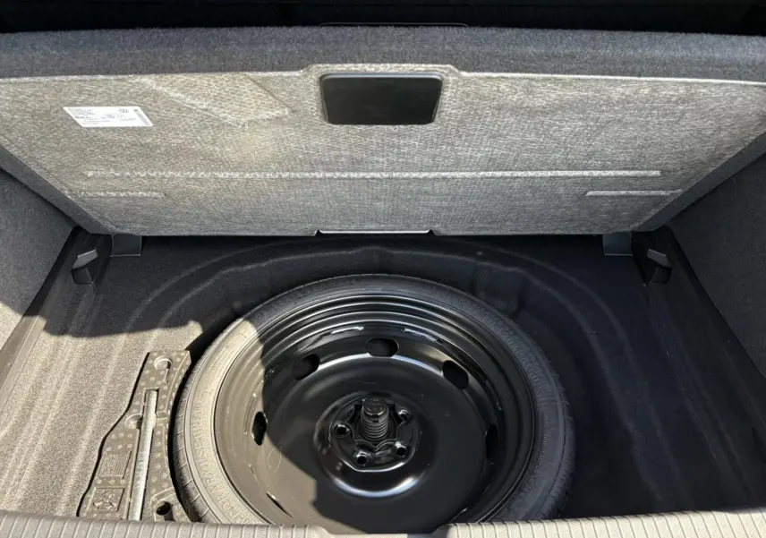 Vue plongeante sur la roue de secours noire dans le coffre d'une Volkswagen Golf VIII 1.5 TSI gris lunaire 2024.