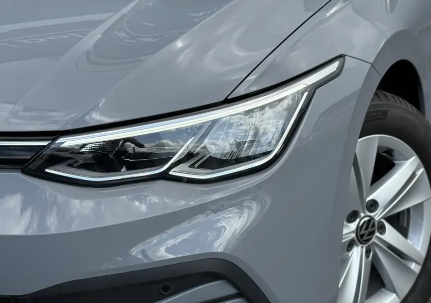 Gros plan sur l'avant droit de la Volkswagen Golf VIII gris lunaire, mettant en valeur son phare LED et sa jante alliage 16 pouces.