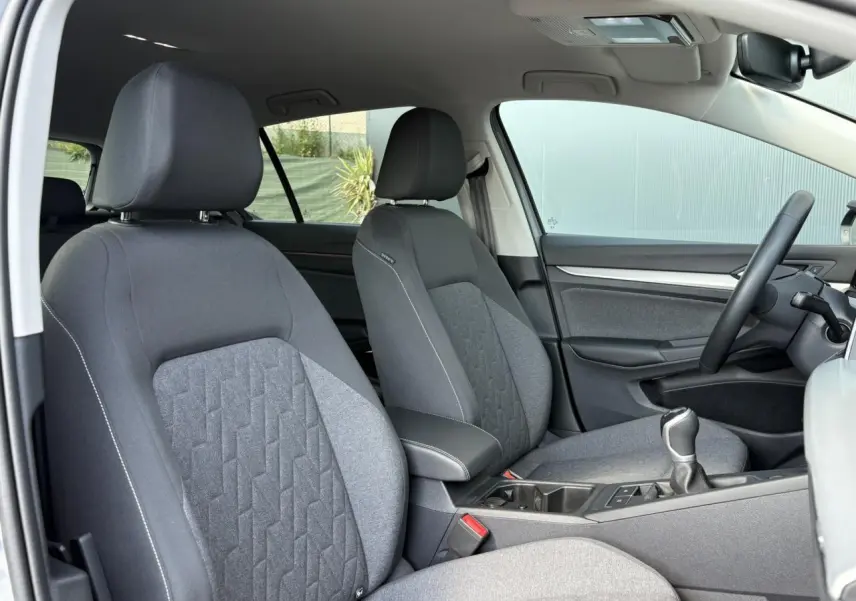 Vue intérieure côté conducteur de la Volkswagen Golf VIII 1.5 TSI 150 Active avec sièges tissu gris et volant multifonction.