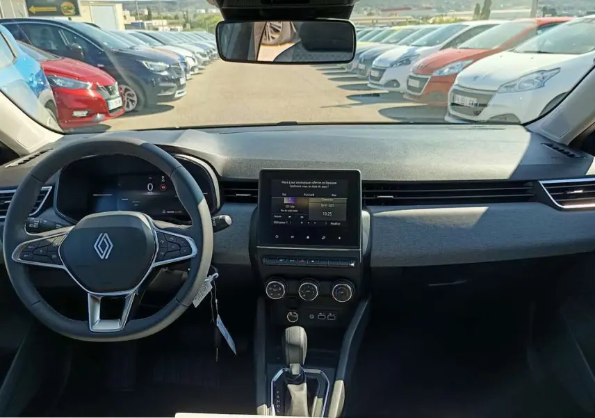 Vue intérieure avant du tableau de bord et volant d'une Renault Clio 2025 gris schiste avec écran tactile central et boîte auto.