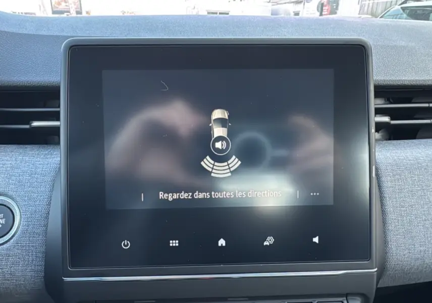 Écran tactile central du tableau de bord de la Renault Clio 2025 gris schiste, affichant l'alerte de surveillance des angles morts.