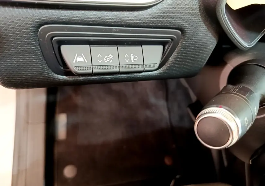 Gros plan sur les commandes d'assistance et réglage des phares du tableau de bord d'une Renault Clio Business blanche.