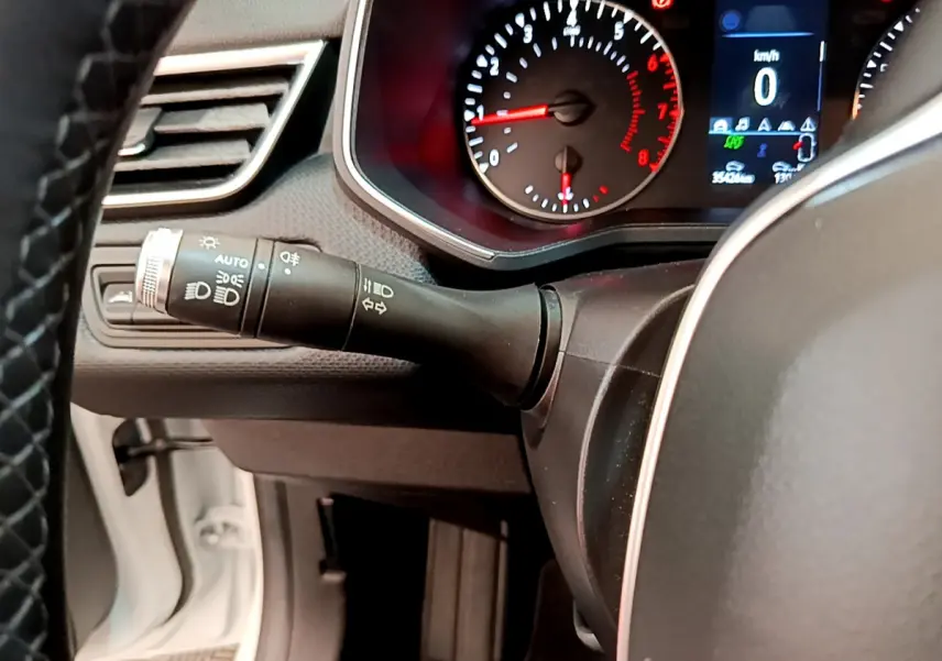 Gros plan sur le tableau de bord et commodo gauche d'une Renault Clio Business blanche, affichage digital et compte-tours visibles.