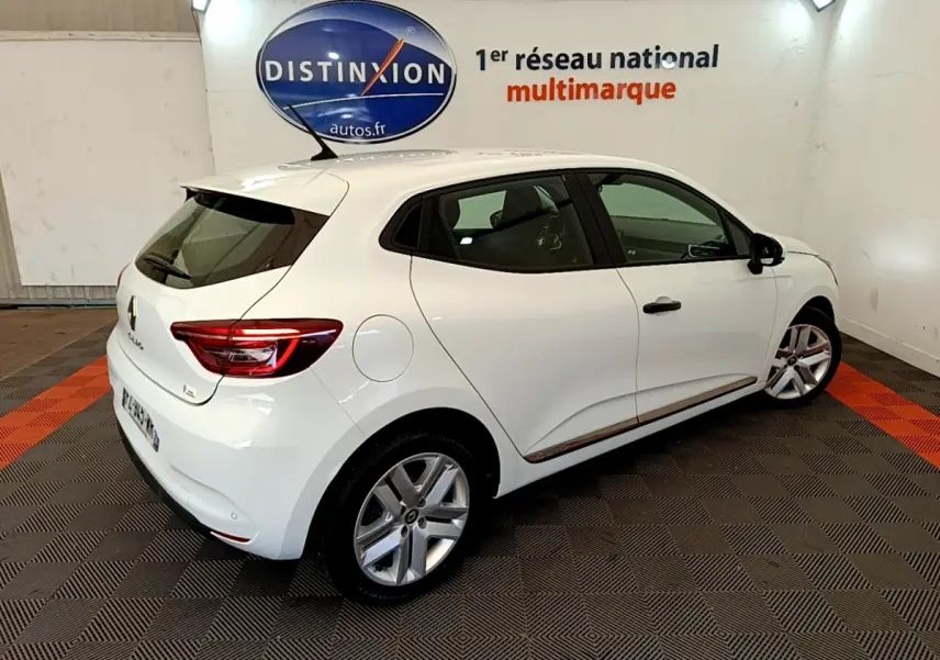 Vue 3/4 arrière droite d'une Renault Clio Business blanche, avec jantes alliage et feux arrière LED visibles dans un showroom.