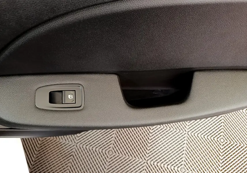 Gros plan sur la poignée intérieure et le bouton de verrouillage de la porte côté conducteur d'une Renault Clio Business blanche.