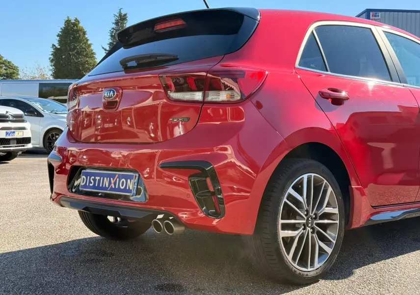 Vue 3/4 arrière droite d'une KIA Rio rouge grenadine 2022 avec double sortie d'échappement et jantes alliage.
