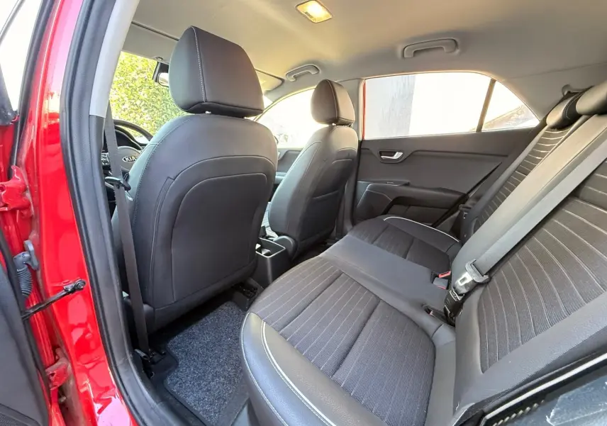 Vue intérieure arrière droit de la Kia Rio rouge grenadine 2022, sièges noirs en tissu et cuir avec ceinture de sécurité.