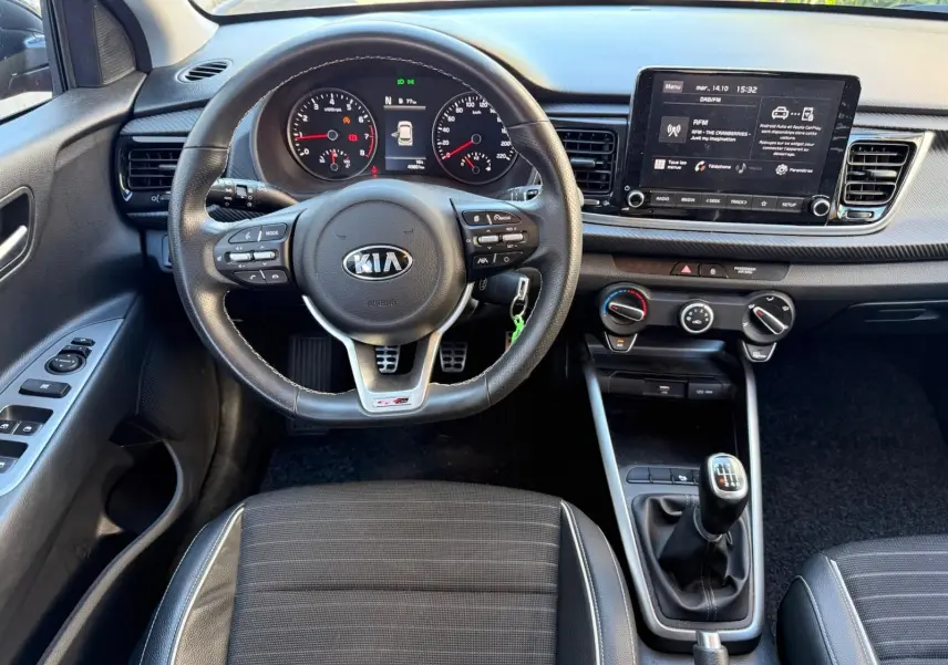 Vue intérieure du poste de conduite de la Kia Rio 2022, volant multifonction et levier de vitesse manuel visibles.