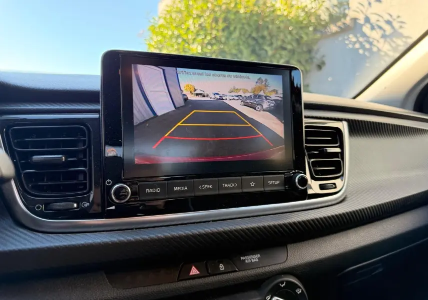 Écran central de la Kia Rio rouge grenadine 2022 montrant la caméra de recul avec guidage de trajectoire en jaune et rouge.