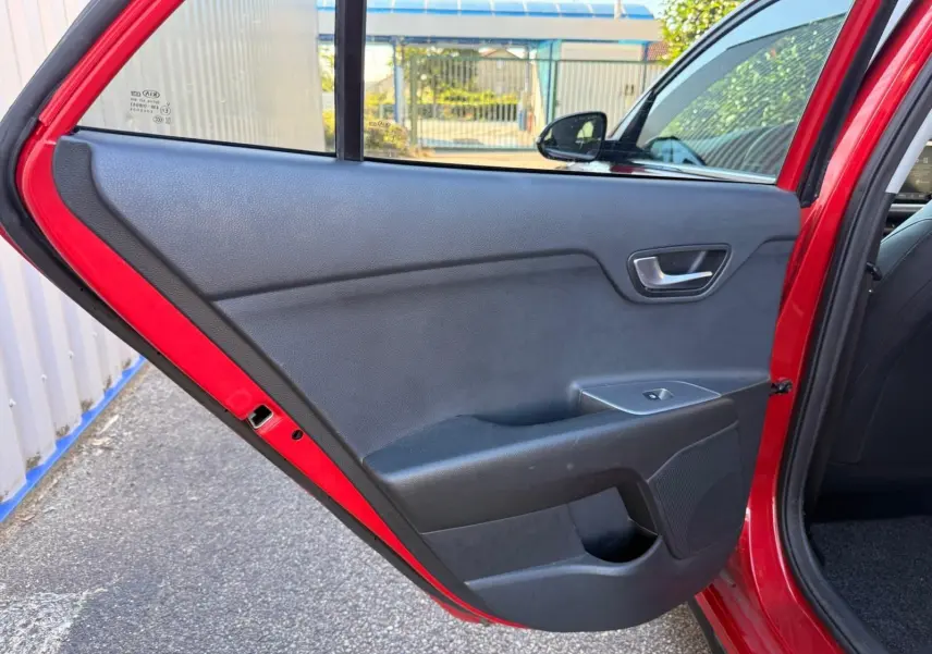 Porte arrière côté gauche ouverte d'une KIA RIO rouge grenadine 2022, intérieur noir avec commande de vitre électrique.
