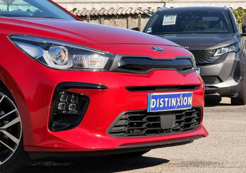 Vue de face en léger 3/4 avant gauche d'une KIA RIO rouge grenadine avec calandre noire et plaque Distinxion.