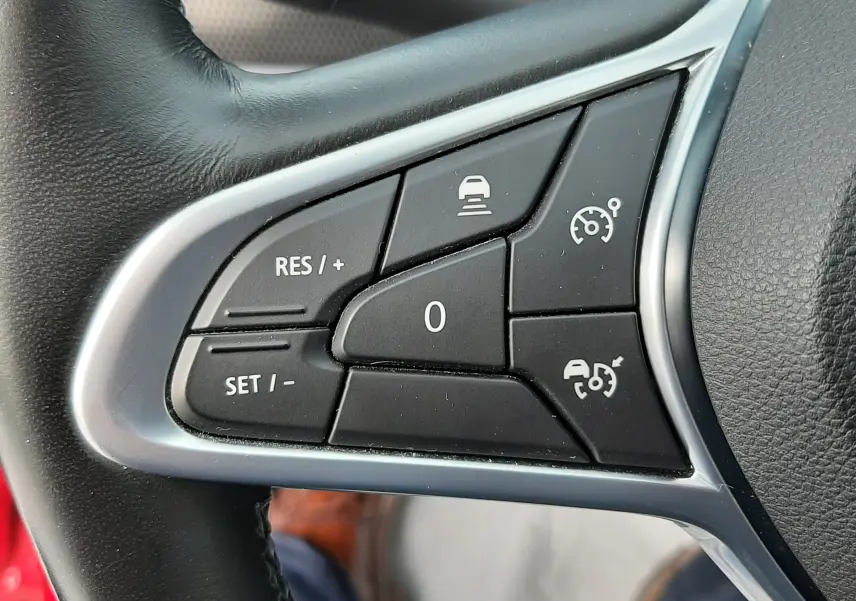 Gros plan sur les commandes au volant côté gauche du Renault Arkana rouge Flame, boutons de régulateur et assistance conduite.