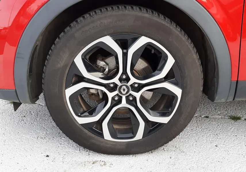 Gros plan sur la roue avant gauche rouge flamme d'un Renault Arkana 1.6 E-TECH avec jante alliage noire et argent.