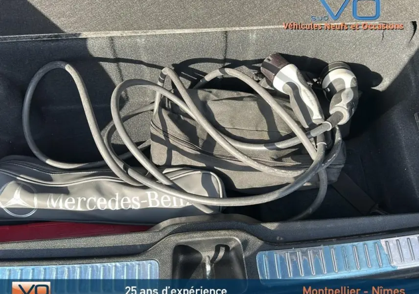 Vue plongeante sur le coffre d'un Mercedes GLC 300 de 2020 avec câble de recharge et sac de marque gris anthracite.