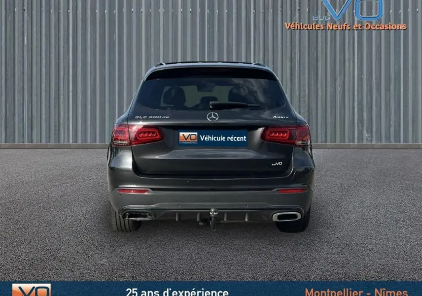 Vue arrière d'un Mercedes GLC 300 de gris anthracite avec attelage et feux arrière allumés sur fond neutre.