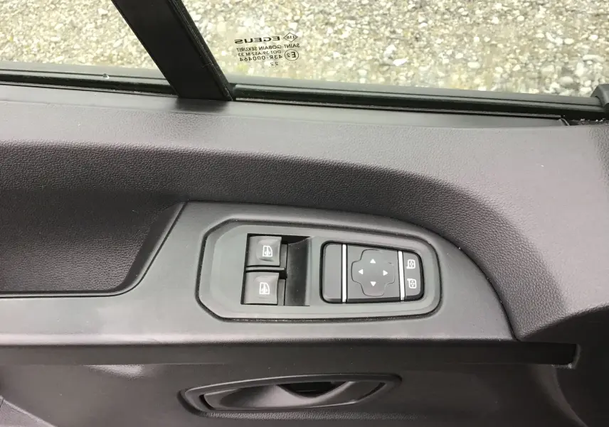 Détail des commandes de lève-vitres et réglage des rétroviseurs sur la porte côté gauche du Renault Trafic Combi gris Comète.