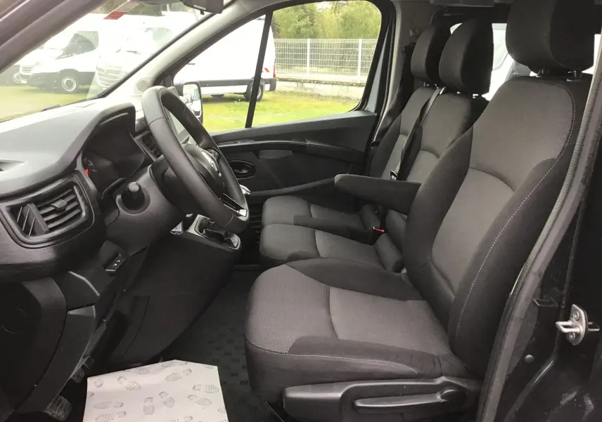 Vue intérieure côté conducteur du Renault Trafic Combi gris comète, montrant les sièges avant et le volant multifonction.