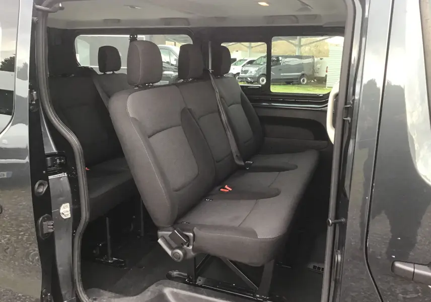 Vue latérale droite du Renault Trafic Combi gris comète montrant les sièges passagers en tissu noir sur trois rangées.