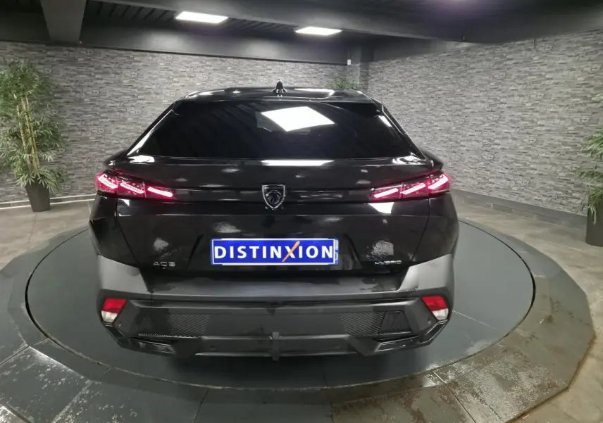 Vue arrière d'une Peugeot 408 noire avec feux arrière LED allumés dans un showroom intérieur.