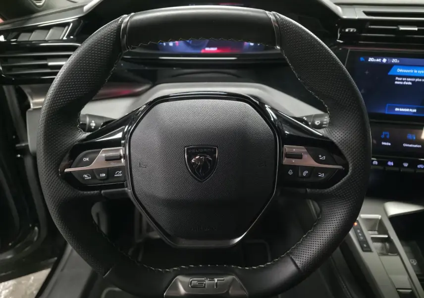 Volant cuir perforé noir avec badge GT au centre, tableau de bord numérique et écran tactile du Peugeot 408 1.6 PHEV 2024.