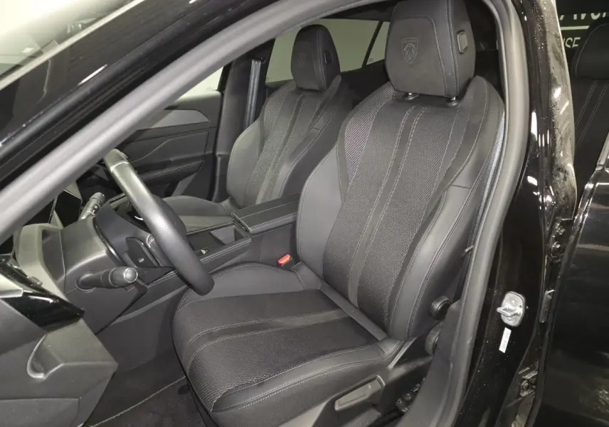 Vue intérieure côté conducteur de la Peugeot 408 noire 2024, sièges sport en tissu et cuir avec logo Peugeot brodé.
