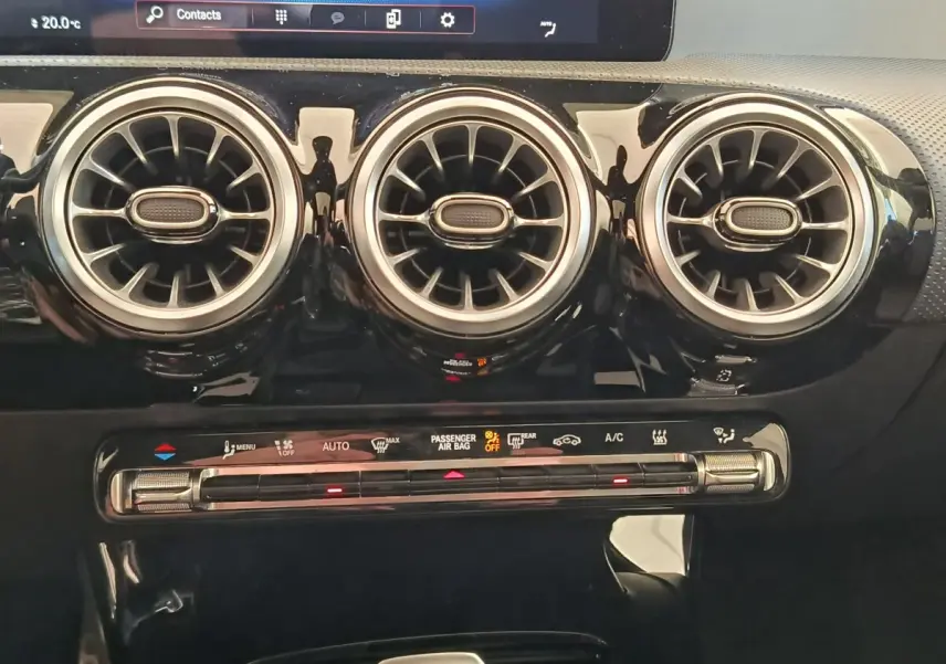 Détail intérieur montrant les trois aérateurs ronds chromés et la commande de climatisation tactile d'une Mercedes Classe A blanche.