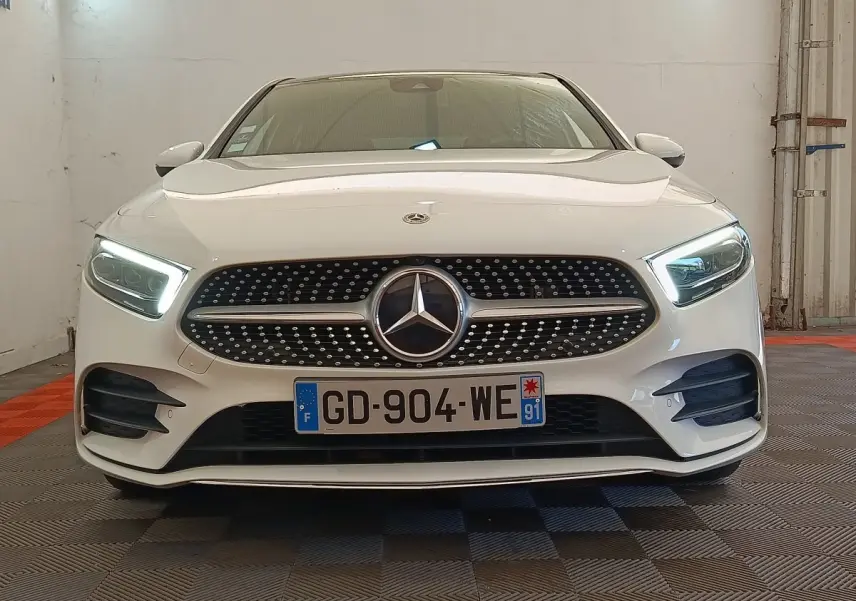 Mercedes Classe A 250 e AMG Line blanche vue de face, phares LED allumés et calandre diamantée distinctive.