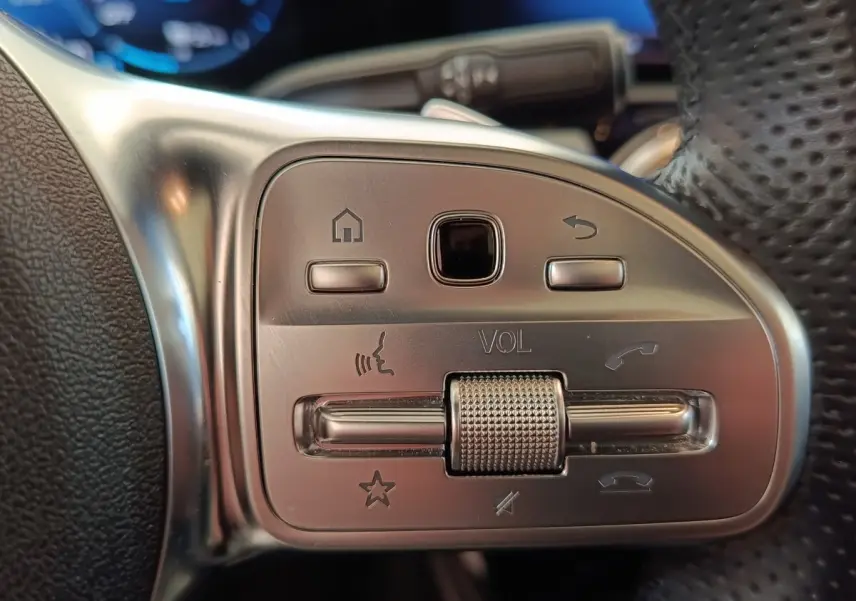 Gros plan sur les commandes en aluminium et cuir du volant multifonctions du Mercedes Classe A blanc, version AMG Line.