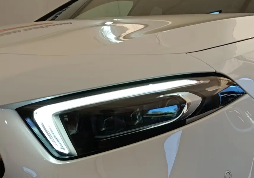 Gros plan sur le phare avant droit LED d’une Mercedes Classe A blanche, soulignant son design moderne et précis.