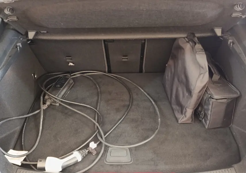 Coffre ouvert d’une Mercedes Classe A 250 e AMG Line blanc, avec câble de recharge et sac de rangement.