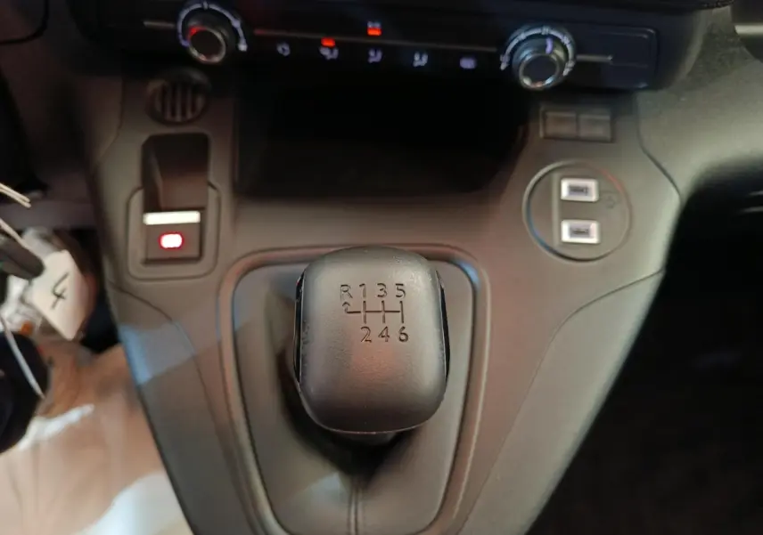 Gros plan sur le levier de vitesses manuel noir du Peugeot Partner blanc, avec commandes de climatisation et ports USB visibles.