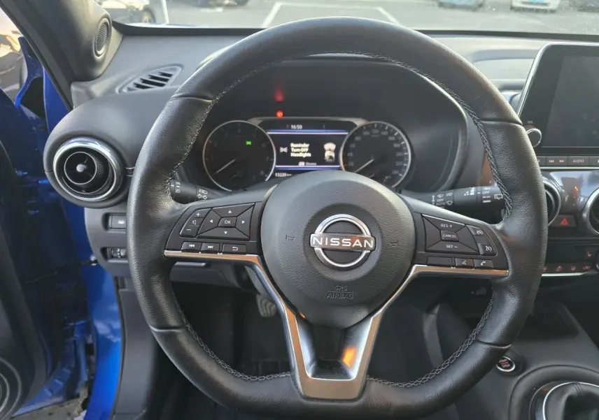 Vue intérieure centrée sur le volant cuir noir du Nissan Juke II bleu magnetic avec tableau de bord digital visible.